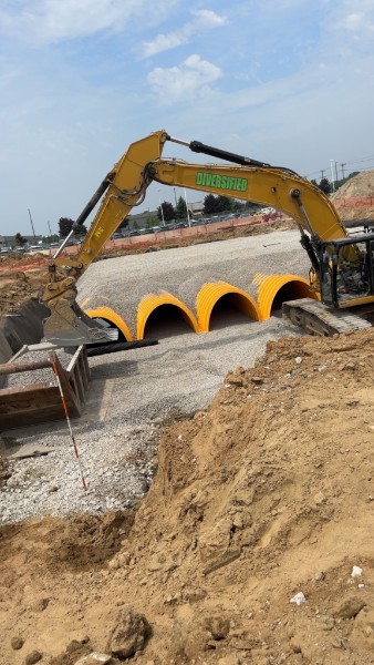Excavator setting large drainage pipe on a prepared site