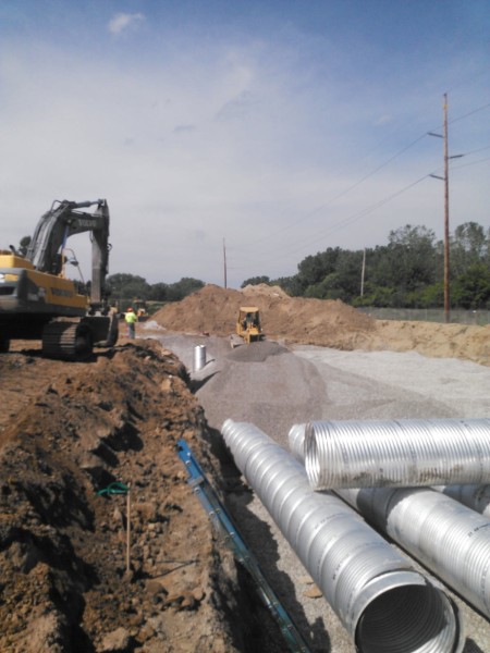 Excavator working beside staged drainage pipe
