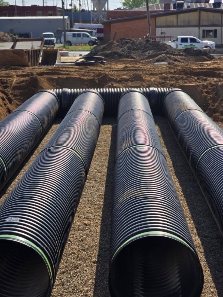 Large black drainage pipe staged in an excavation